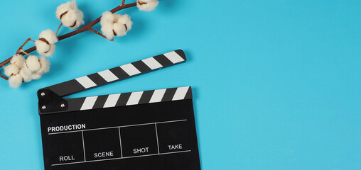 Black clapper board and cotton flowers on blue background.