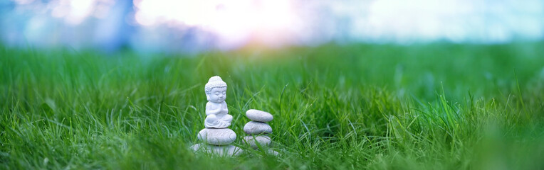 little Buddha statue and spa stones in green grass, abstract natural background. Buddhism culture symbol. esoteric spiritual practice, meditation. harmony, relax, life balance concept. long banner