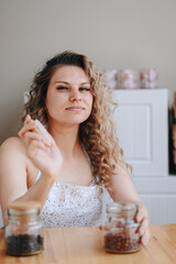 Vertical Portrait of Curly Housewife. girl in an apron holds jar of coffee. Bank with tea