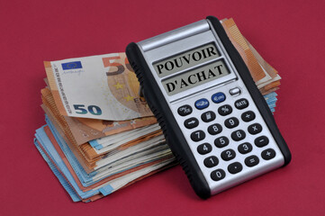 Concept de pouvoir d'achat avec une calculatrice posée sur des billets de banque en euros sur fond rouge