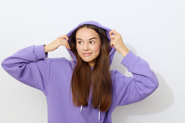 Fototapeta na wymiar an interested woman is standing on a white background in a purple tracksuit wearing a hood on her head with her hands on it looking around