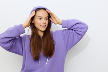 Naklejka premium an interested woman is standing on a white background in a purple tracksuit wearing a hood on her head with her hands on it looking around
