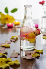 Selbstgemachtes duftendes Rosenwasser in einer Glasflasche mit Blütenblätter einer Rose in Gelb und Rosa