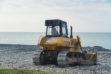 Yellow excavator working on the pebbled beach near the seashore. High quality photo