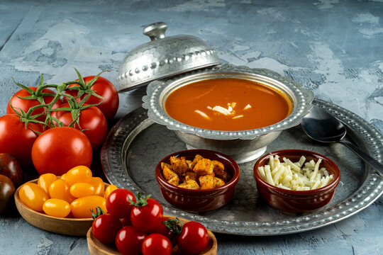 Bowl with tomato soup and ingredients, tomata soup in a metal bowl served with cheeese and croutons and different color of fresh  tomatoes