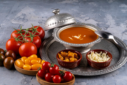 Bowl with tomato soup and ingredients, tomata soup in a metal bowl served with cheeese and croutons and different color of fresh  tomatoes