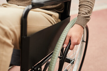 Close-up of unrecognizable invalid sitting in wheelchair and turning handrails of wheelchair...