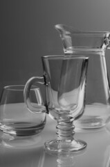 a glass cup, a jug and a glass mug stand empty on a gray background