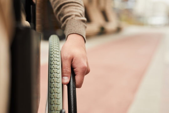 Close-up of unrecognizable man in sweater learning to use wheelchair: he twisting handrails of wheelchair