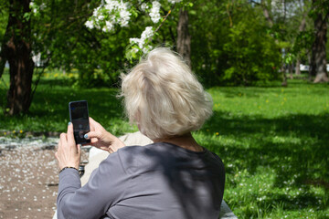 A gray-haired woman sits on a bench and takes pictures on the phone