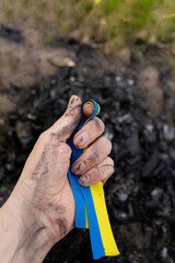 the symbol of ukraine is clutched in the hand against the background of coals from the conflagration. ukraine on fire, struggle for freedom in ukraine. yellow blue ribbon of the flag of ukraine