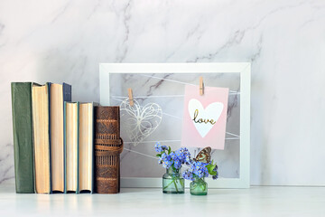 beautiful home interior composition with butterfly on blue flowers, old books and decorative frame on table, abstract marble background. Relax time, harmony. romantic inspiration composition