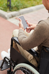 Fototapeta na wymiar Close-up of wheelchair-bound man checking phone while resting outdoors during stroll in city