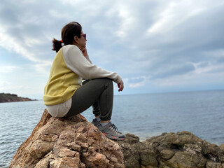 Naklejka na ściany i meble Woman sitting on rocks at the seaside daydreaming