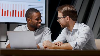 Smiling businessmen working with statistics using laptop and multimedia tv in office