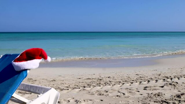 Footage of the beautiful beach in Cuba Varadero, showing a red Christmas Santa hat being placed on the side of a blue sun lounger, Christmas in the sun and beach concept, filmed in 8K quality