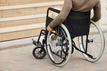 Close-up of unrecognizable crippled man in sweater turning handrails while moving wheelchair...