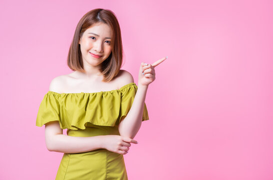 Image of young Asian woman wearing green dress on pink background