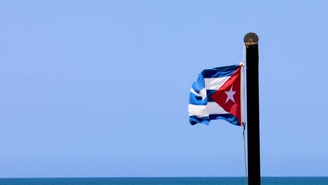 A Cuban flag blowing in the wind in the town of Varadero in Cuba with clear blue Skys and the clean ocean waters behind filmed in 8k Quality
