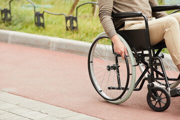 Fototapeta premium Close-up of unrecognizable guy in casual clothing sitting in modern wheelchair and rotating wheel of wheelchair for motion outdoors