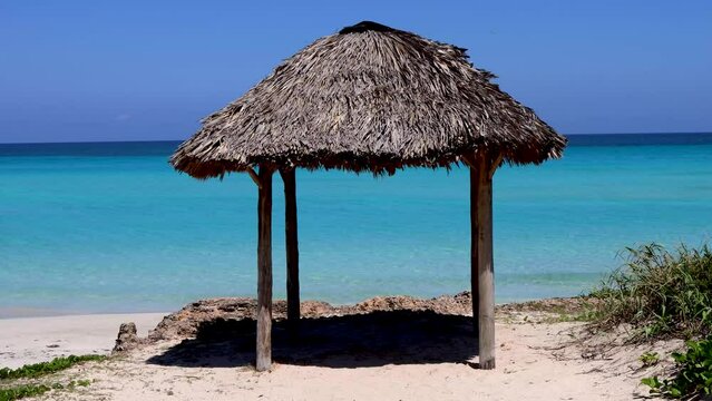 The beautiful beach front of the Cuban beach at Varadero in Cuba showing a wooden sun shade shack by the ocean, filmed in 8k footage in the summer time on a sunny summers day.