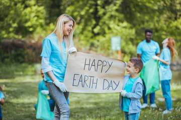 Happy Earth day! People cleaning up litter on grass. Group of international young people building team outdoor in park. Volunteer together pick up trash in the park