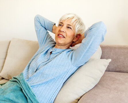 Happy mature woman relaxing at home reclining on comfortable sofa with hands behind head looking upwards with a dreamy smile of pleasure. Woman having a daydream on sofa relaxing with head tilted back