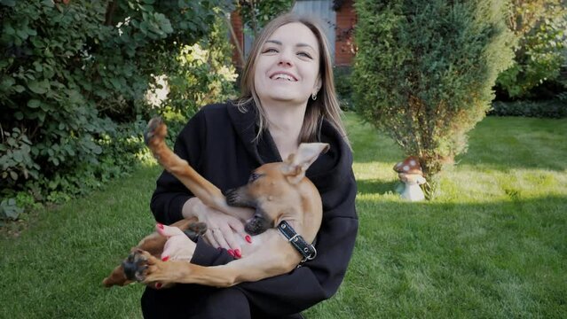Happy woman with hugs funny puppy of a German boxer in the backyard, a crazy dog breaks out of her hands and indulges