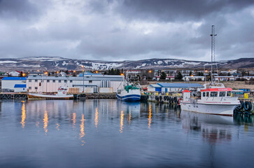 Fototapeta na wymiar Hvammstangi, Iceland, April 30, 2022: view of the town's harbour area, with various boats and sheds, during evening twilight
