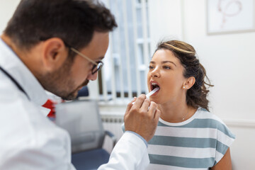 Obraz na płótnie Canvas Doctor using inspection spatula to examine patient throat. ENT doctor doing throat exam of a woman. patient opened her mouth to throat check-up