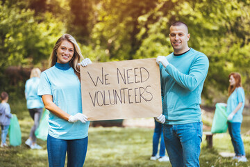 Group of young adults collaborate to organize a recycling campaign. Man and woman foreground with sign. They holds poster that she made.....