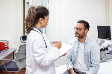 Fototapeta premium Serious man consulting with young female physician doctor at checkup meeting in hospital. Skilled general practitioner giving healthcare medical advices to patient.