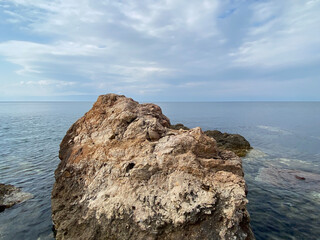 rocks on sea background. Dark rock in a blue ocean under cloudy sky in beautiful weather - Powered by Adobe