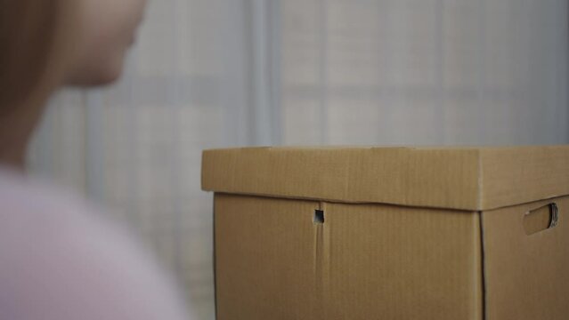 The hand of woman is using a scissors to cut the white plastic seal that locks the brown cardboard box to retrieve the archives of important documents, protecting information.