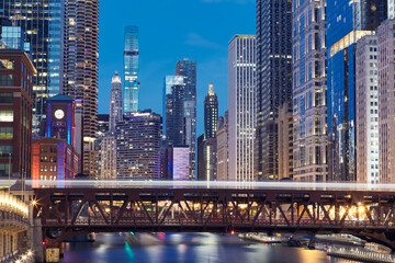 Railway bridge over Chicago River amidst illuminated city. Urban skyline with skyscrapers at night. .