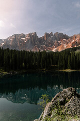Fototapeta na wymiar Vertical photo of a lake in the middle of the nature in the Dolomites, surrounded by trees, hill, mountains and snow. The water of the lake is clean and transparent. Refrection of the mountain.