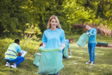 The young adult woman, who is one of a diverse group of volunteers, takes time to smile for the camera. Hold garbage bag and looking at camera