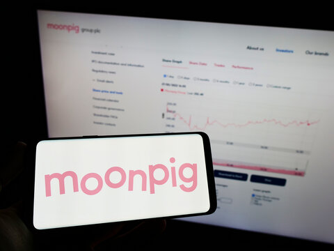 Stuttgart, Germany - 05-28-2022: Person holding mobile phone with logo of greeting card company Moonpig Group plc on screen in front of business web page. Focus on phone display.