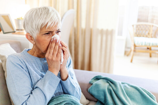 Shot of a senior woman blowing her nose with a tissue at home. Senior woman blowing her nose while feeling sick at home.