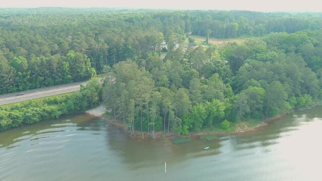 stunning aerial footage of the rippling green waters of Lake Acworth surrounded by lush green trees, grass and plants with cars driving on the highway at Proctor Landing Park in Acworth Georgia USA