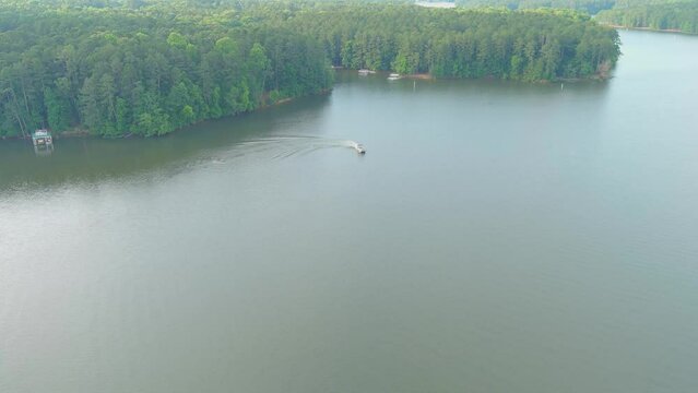 aerial footage of the rippling blue waters of Lake Acworth surrounded by lush green trees, grass and plants with a motor boat on the water with blue sky and clouds at Proctor Landing Park in Acworth
