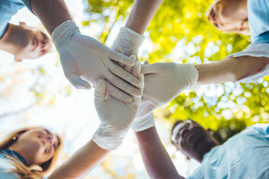 The concept of volunteering, unity and care for the environment. Group of young volunteers in protective gloves greetings before cleaning the park, close-up, low angle view