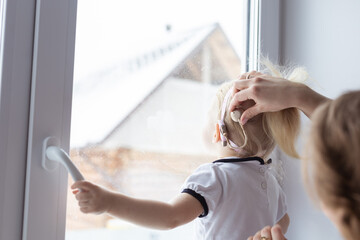 Mother helps her deaf baby daughter putting hearing aid in little girl's ear indoors - cochlear...