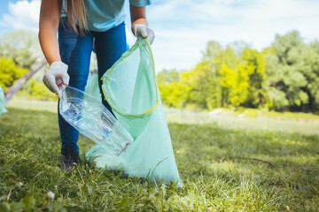 An unrecognizable woman cleans the park of garbage. An unrecognizable young volunteer collects...