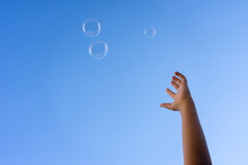 Hand of a child trying to catch some soap bubbles that rise to the sky