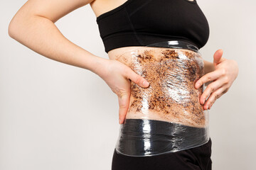 A woman makes a belly wrap with a coffee anti-cellulite body scrub. The concept of weight loss and...