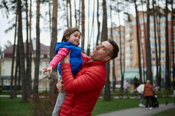 Handsome Caucasian man - loving dad tosses his daughter - a little cute girl high up in a city park. Family and father's day, love, parents, children