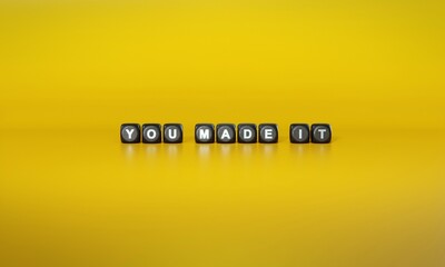 Words ‘You made it’ spelled out in white text on dark wooden blocks against plain yellow background. 3D rendering