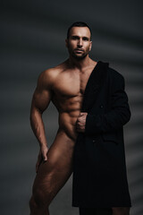 Naked handsome man with coat covered half of his body. Fashion naked male model.