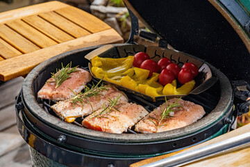 grilling salmon, paprica and cherry tomatoes on a ceramic grill with charcoal in the garden at a winter day in the outdoor